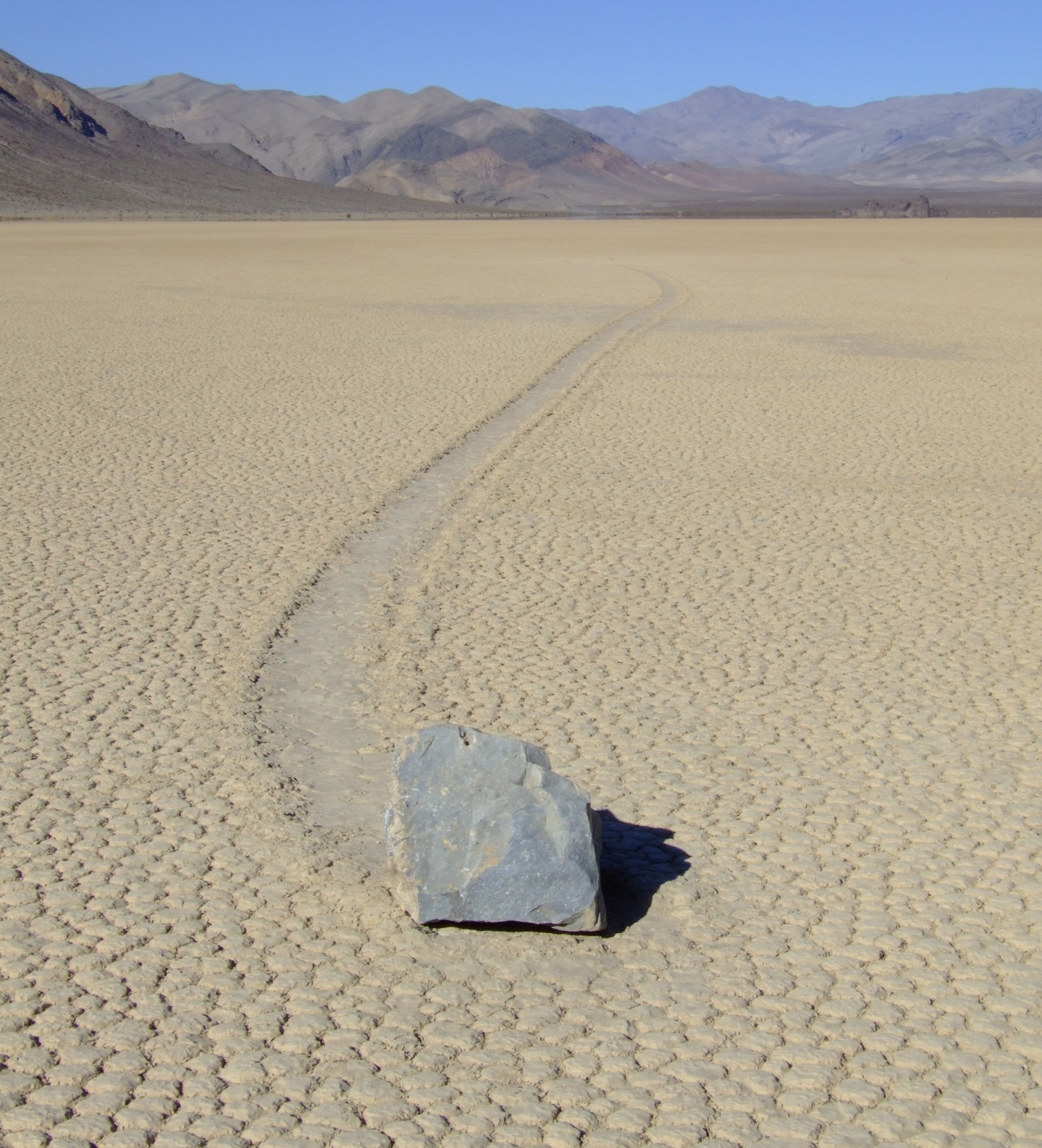 Bongkah batu belayar di Racetrack Playa dengan alur jejak panjang di atas tanah merekah